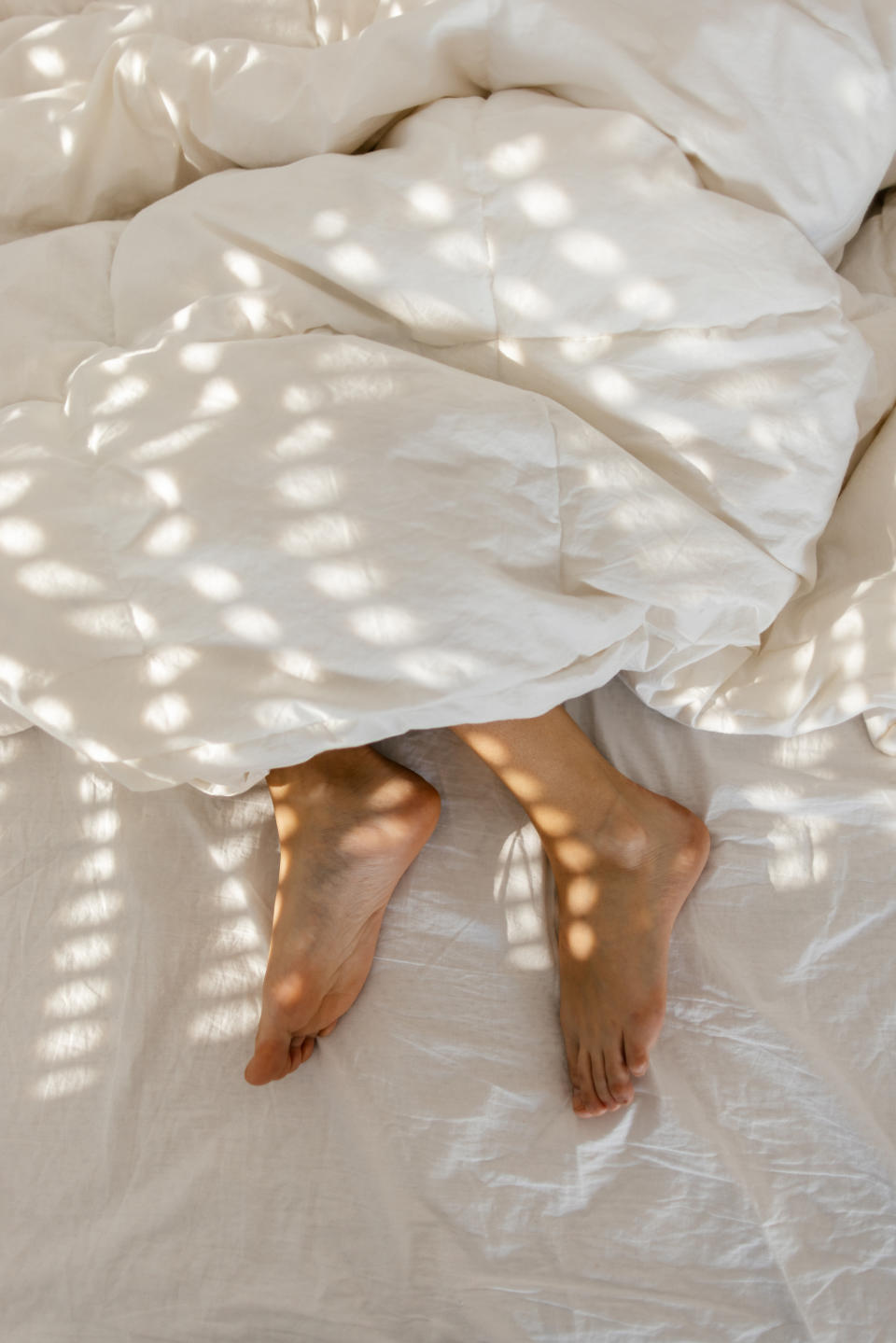 Person's bare feet sticking out from under a light blanket with sunlight filtering through