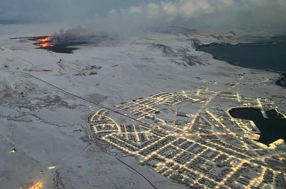 The evacuated Icelandic town of Grindavik (R) is seen as smoke billow and lava is thrown into the air from a fissure during a volcanic eruption on the Reykjanes peninsula 3 km north of Grindavik, western Iceland on December 19, 2023 (AFP via Getty Images)