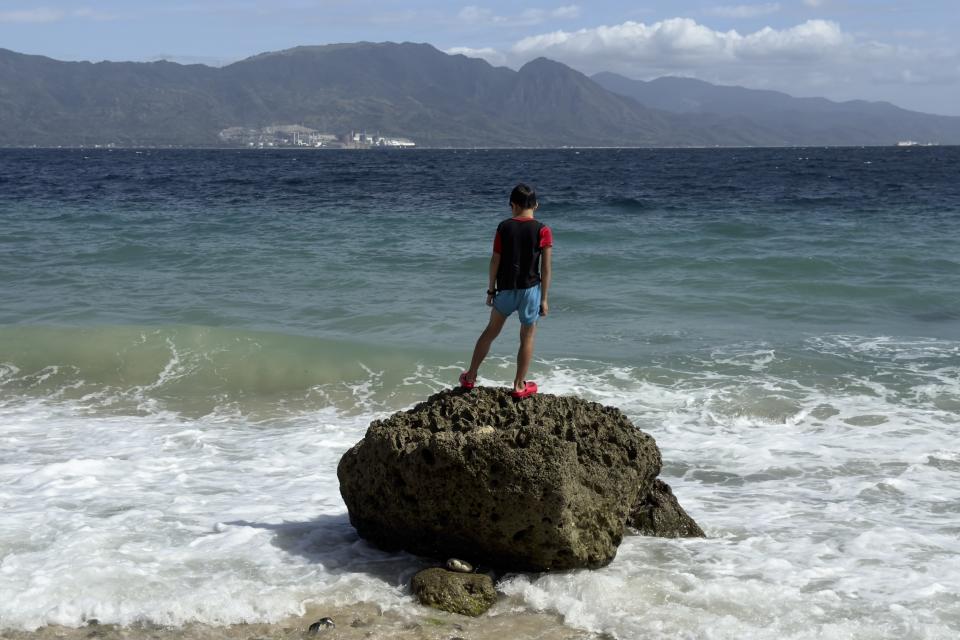 A boy stands on a rock on Verde Island opposite the Ilijan Liquified Natural Gas plant in Batangas province, Philippines on Thursday, Jan. 25, 2024. The Philippines is seeing one of the world's biggest buildouts of natural gas infrastructure. This could impact nearby coral reefs and fishing communities. (AP Photo/Aaron Favila)