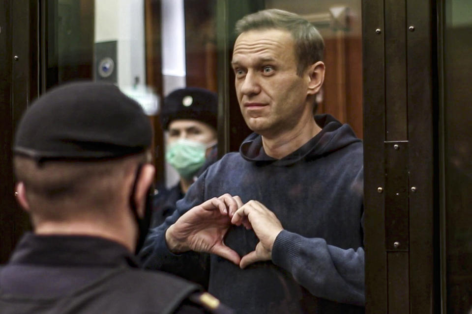 FILE - In this file photo made from video provided by the Moscow City Court on Wednesday, Feb. 3, 2021, Russian opposition leader Alexei Navalny makes a heart gesture standing in a cage during a hearing in Moscow, Russia. In a span of a decade, Navalny has gone from the Kremlin's biggest foe to Russia's most prominent political prisoner. Already serving two convictions that have landed him in prison for at least nine years, he faces a new trial that could keep him behind for another two decades. (Moscow City Court via AP, File)