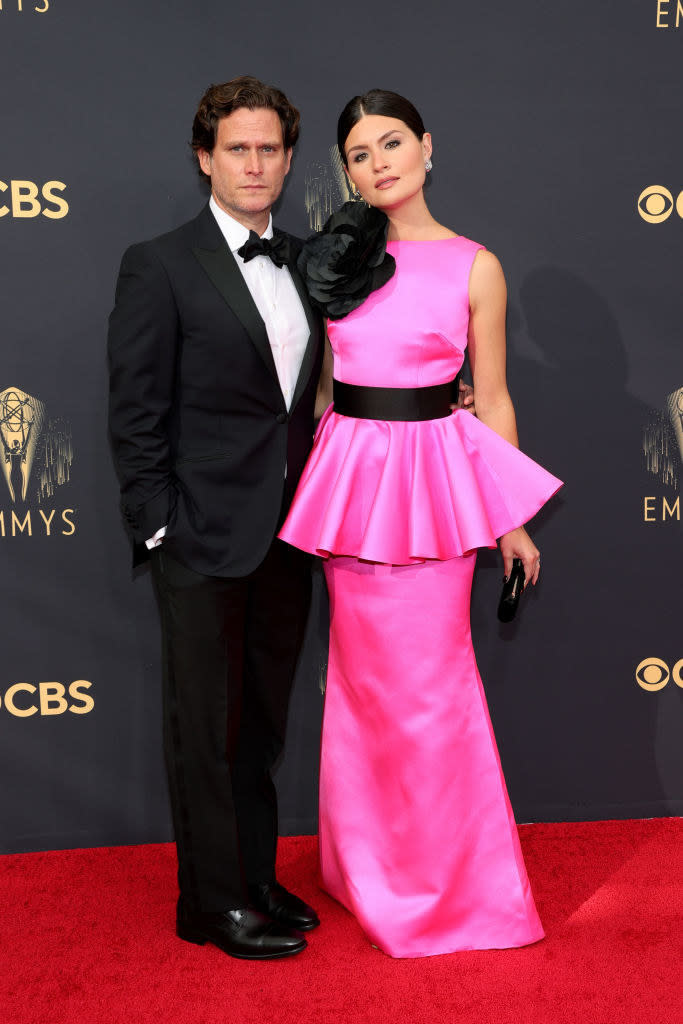 Phillipa Soo wears a brightly colored gown with a ruffle skirt around the middle and Steven Pasquale wears a dark suit