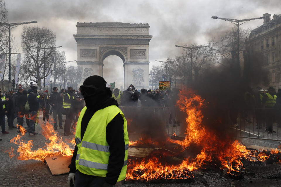 A yellow vest protester walks past a fire on the Champs Elysees avenue Saturday, March 16, 2019 in Paris. French yellow vest protesters clashed Saturday with riot police near the Arc de Triomphe as they kicked off their 18th straight weekend of demonstrations against President Emmanuel Macron. (AP Photo/Christophe Ena)