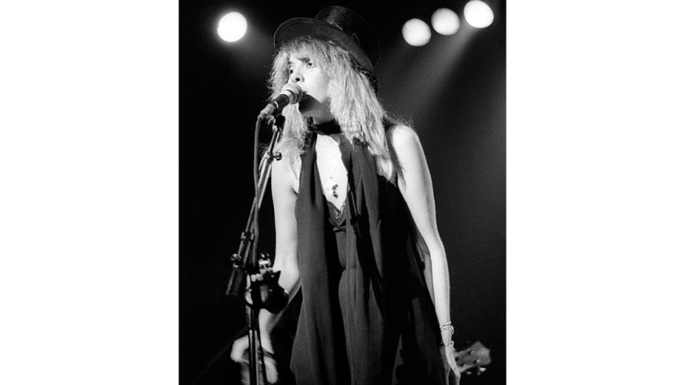 Stevie Nicks singing on stage wearing hat and skinny scarf