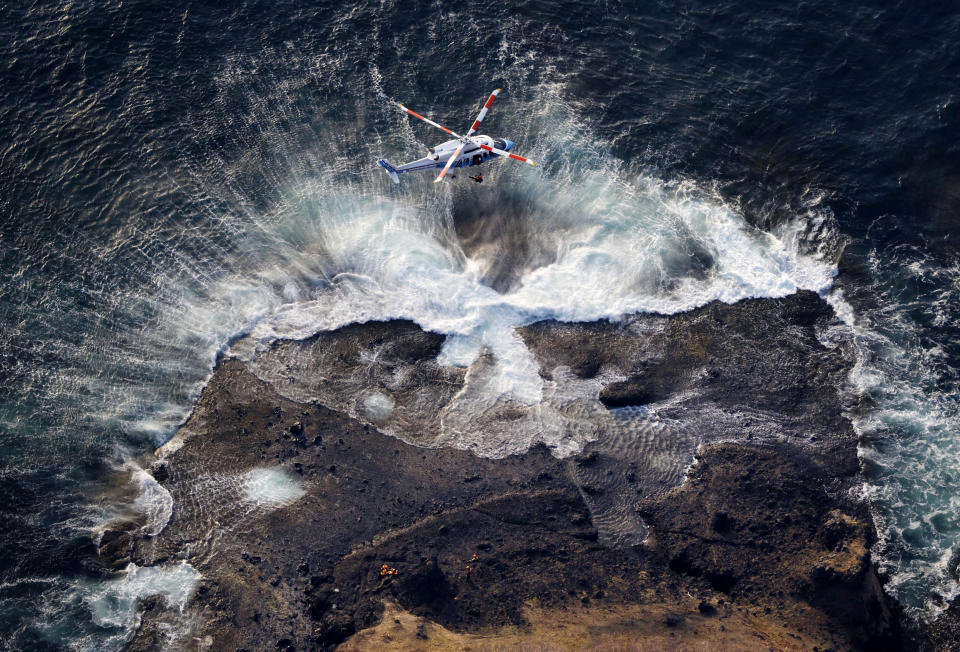 This aerial photo shows a rescuer being lifted in a search operation for missing passengers and crew members of a sunken tour boat, off Shiretoko Peninsula, northern Japan of Hokkaido Sunday, April 24, 2022. (Masanori Takei/Kyodo News via AP)