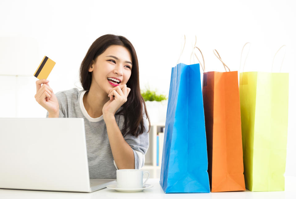 A young woman holding her credit card as she gazes at shopping bags.