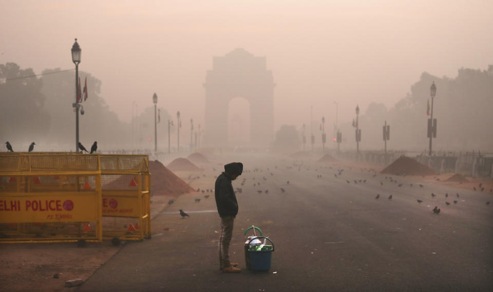 In this Wednesday, Dec. 26, 2018, photo, a boy selling tea awaits customers early morning amidst smog in New Delhi, India. Authorities have ordered fire services to sprinkle water from high rise building to settle dust particles and stop burning of garbage and building activity in the Indian capital as the air quality hovered between severe and very poor this week posing a serious health hazard for millions of people. (AP Photo/Manish Swarup)