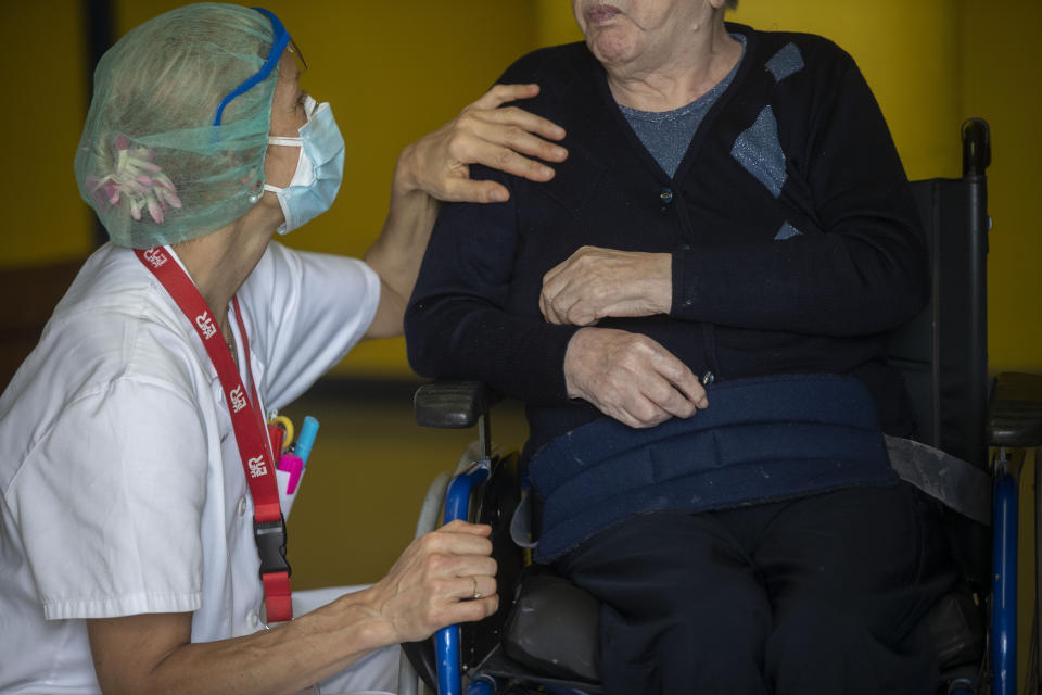 Maria Giulia Badaschi, health director, at the Martino Zanchi Foundation nursing home places her hand on the shoulder of Laura Ricardi, 86, as she sits in a wheelchair at a safe distance to talk to her family in Alzano Lombardo, Italy, Friday, May 29, 2020. (AP Photo/Luca Bruno)
