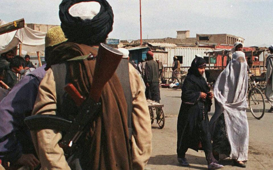 Two Afghan women wearing different styles of Burqas, pass by an armed fundamentalist Taliban militia soldier.