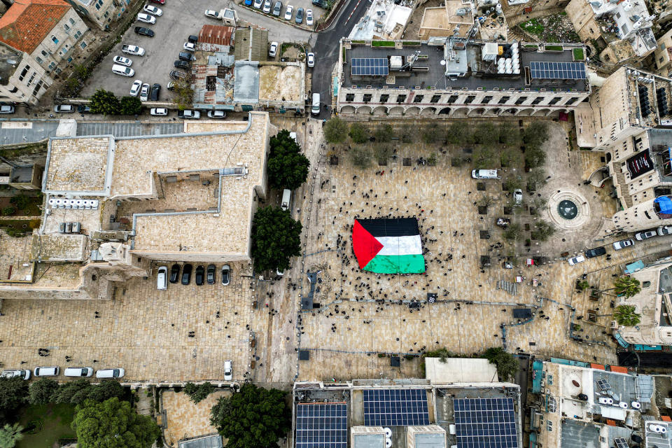 A Palestinian flag is unfurled as people gather at the Manger Square in Bethlehem on Christmas Eve.  (Hazem Bader  / AFP - Getty Images)