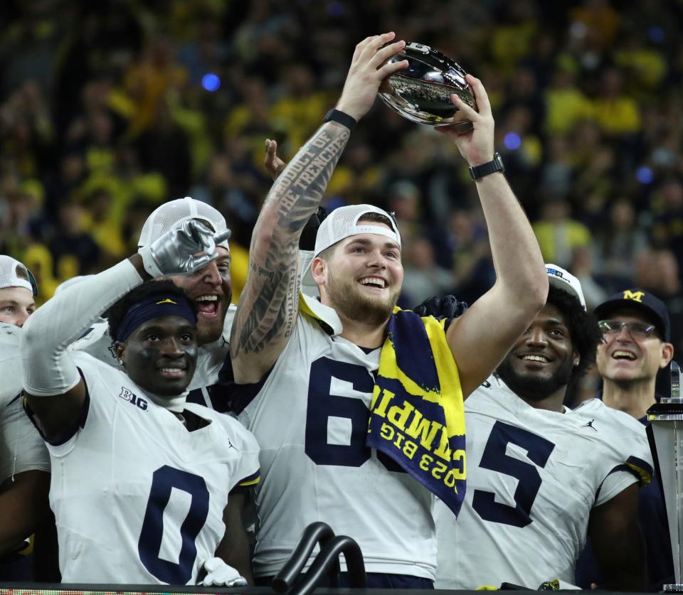 (From left) Michigan defensive back Mike Sainristil, offensive lineman Zak Zinter and defensive end Josaiah Stewart raise the trophy after U-M's 26-0 win over Iowa in the Big Ten championship game on Saturday, Dec. 2, 2023, in Indianapolis.
