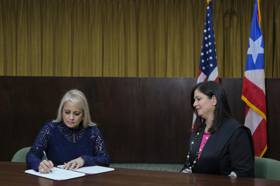 Justice Secretary Wanda Vazquez signs a document after she was sworn in as governor of Puerto Rico by Supreme Court Justice Maite Oronoz, right, in San Juan, Puerto Rico, Wednesday, Aug. 7, 2019 in San Juan Puerto Rico. Vazquez took the oath of office early Wednesday evening at the Puerto Rican Supreme Court, which earlier in the day ruled that Pedro Pierluisi's swearing in last week was unconstitutional. Vazquez was joined by her daughter Beatriz Diaz Vazquez and her husband Judge Jorge Diaz. (AP Photo/Dennis M. Rivera Pichardo)