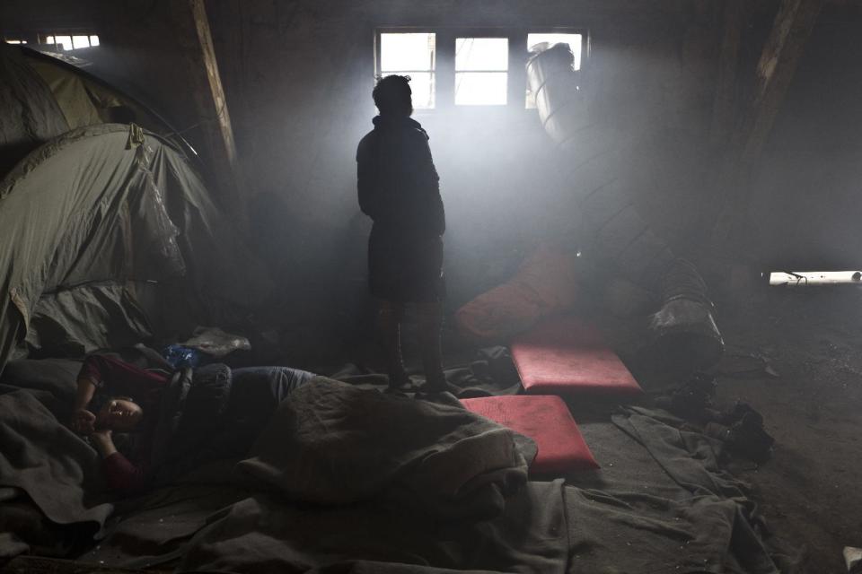 An Afghan refugee man sleeps on the ground while another looks out a window in an abandoned warehouse where they and other migrants took refuge in Belgrade, Serbia, Wednesday, Feb. 1, 2017. Hundreds of migrants have been sleeping rough in freezing conditions in central Belgrade looking for ways to cross the heavily guarded EU borders. (AP Photo/Muhammed Muheisen)