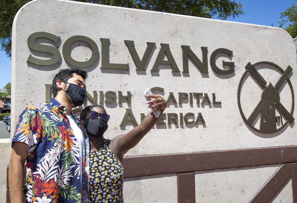 A couple takes a selfie on a Copenhagen Drive sidewalk on July 4, 2020, in Solvang, California. It was almost two weeks ago that the popular California tourist town of Solvang made headlines when it said it wouldn't enforce California Gov. Gavin Newsom's tough new stay-at-home orders. But that was a week before a new City Council took over and told everyone to obey the rules to save lives. (George Rose/Santa Ynez Valley Star via AP)