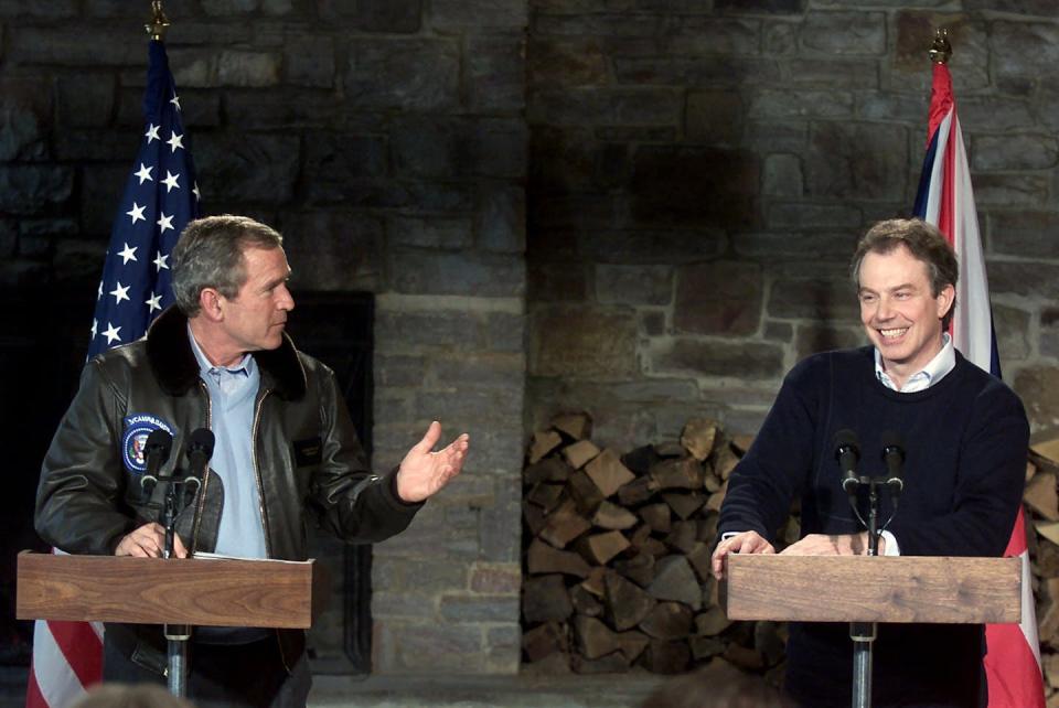 Two men stand a podiums smiling with US and UK flags behind them