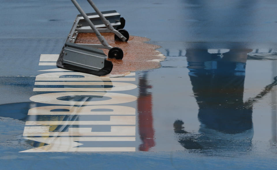 Ground staff clear and dry the outside courts after rain delayed play during a second round singles match at the Australian Open tennis championship in Melbourne, Australia, Thursday, Jan. 23, 2020. (AP Photo/Andy Wong)