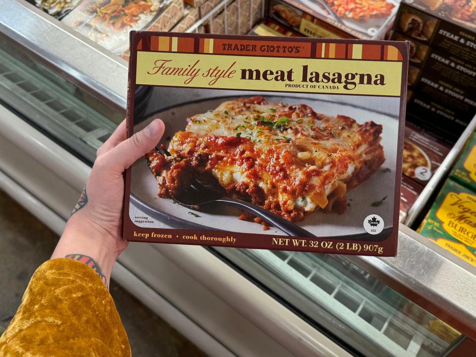 hand holding a box of frozen lasagna in the freezer aisle at trader joes