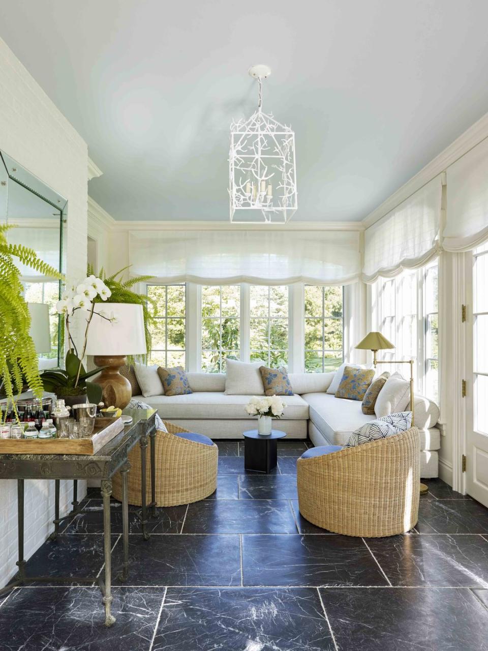 a sunroom with tall banks of windows and stone flooring and a blue ceiling with a sofa and pair of rattan chairs