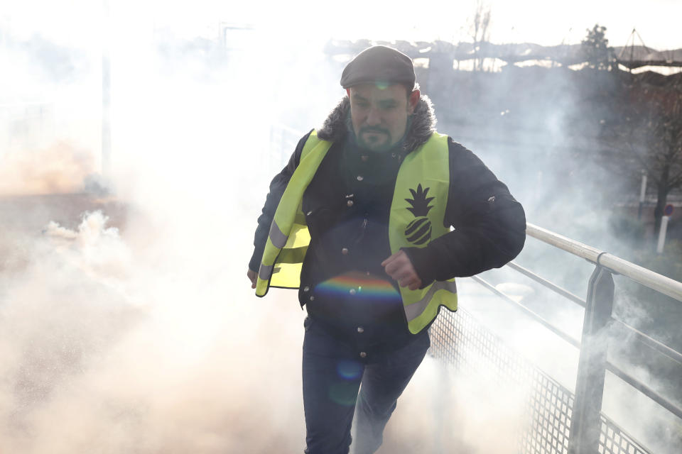A protestor runs from teargas launched by riot police during a demonstration of unionist and yellow vests, in Creteil, outside Paris, Wednesday, Jan. 9, 2019. About 200 protesters, including unionists and yellow vests, gathered Wednesday in Creteil, a Paris suburb, as Macron was doing a visit in a facility dedicated to handball. Some scuffles broke out with police forces that used tear gas to keep the crowd at a distance from the French leader. (AP Photo/Thibault Camus)