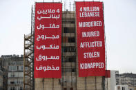 Workers set giant banners on a building that was damaged during last year's massive seaport explosion during a commemoration in Beirut, Lebanon, Wednesday, Aug. 4, 2021. Lebanon is marking one year since the horrific explosion at Beirut port. The grim anniversary Wednesday comes amid an unprecedented economic and financial meltdown and a political stalemate that has kept the country without a functioning government for a full year. (AP Photo/Hussein Malla)