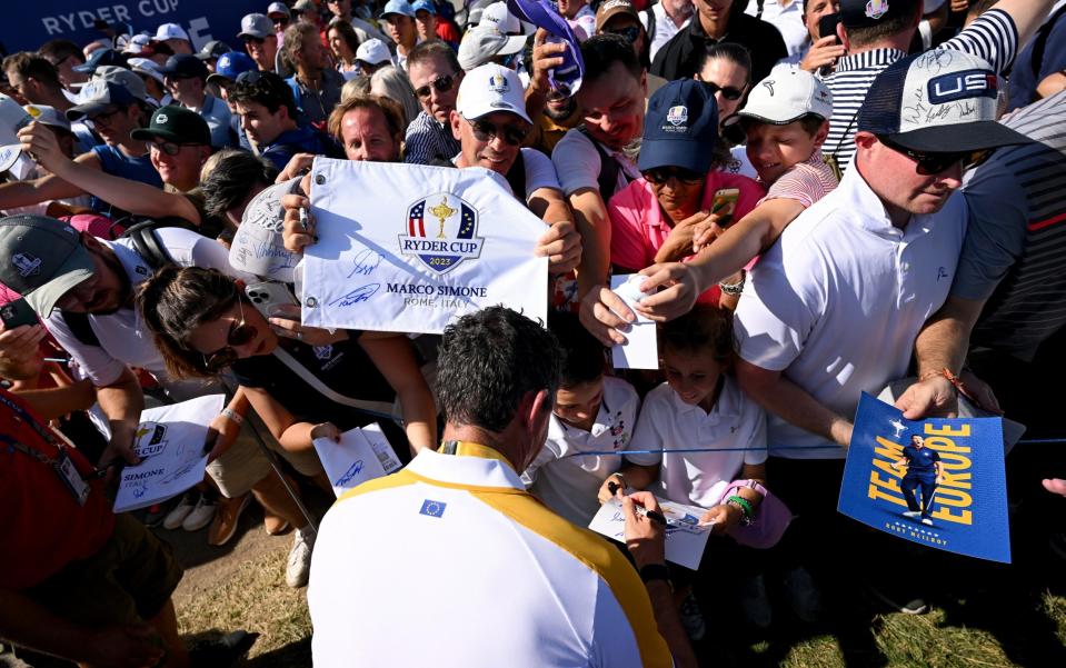 Rory McIlroy of Team Europe signs autographs for fans on the 18th hole during a practice round