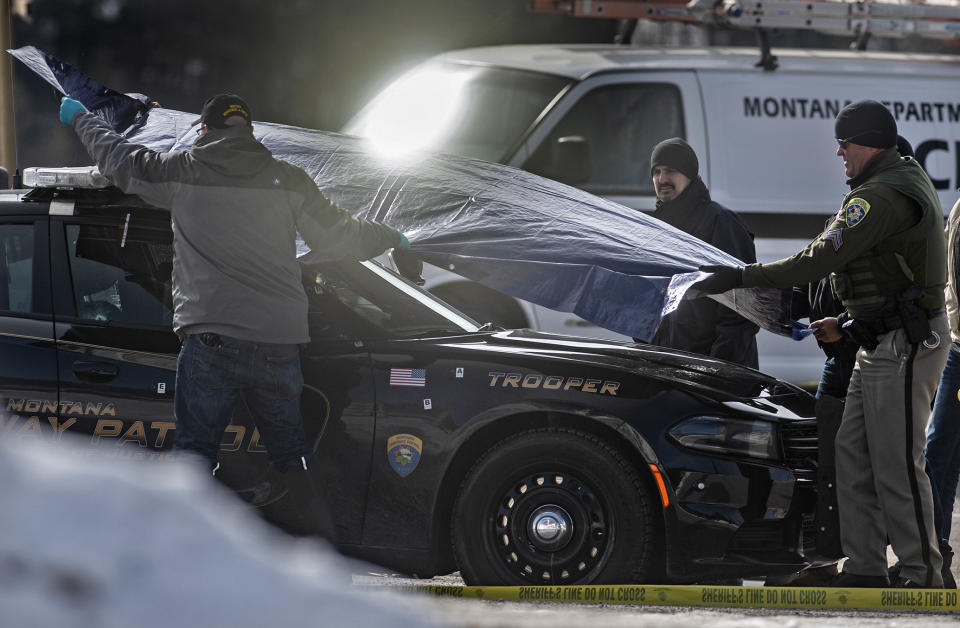 Law enforcement cover Montana State Trooper Wade Palmer's car at the scene of the shooting near the Evaro Bar on Friday, March 15, 2019, in Missoula, Mont. Palmer, who was investigating an earlier shooting, was himself shot and critically injured early Friday after finding the suspect's vehicle, leading authorities to launch an overnight manhunt that ended in the arrest of a 29-year-old man, officials said. (Tommy Martino/The Missoulian via AP)
