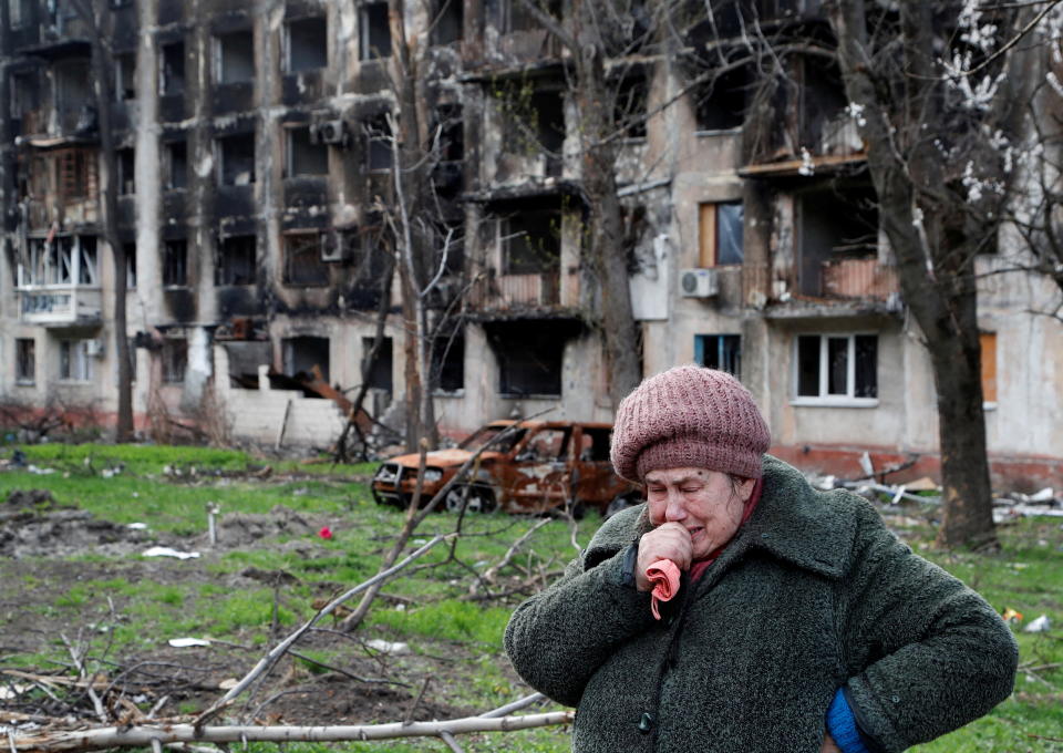 A woman crying in front of a destroyed apartment building.