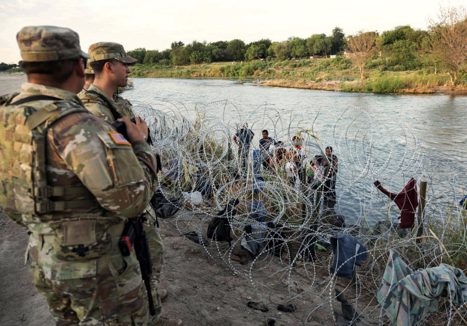 Members of the National Guard look on as migrants try to find a way past razor wire (Andrew Caballero-Reynolds / AFP via Getty Images file)