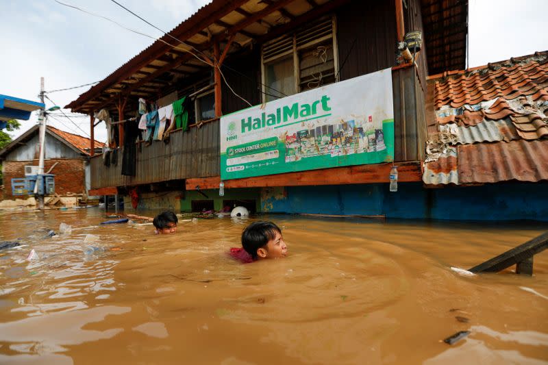 Men swim as they collect items from their houses, flooded after heavy rains in Jakarta