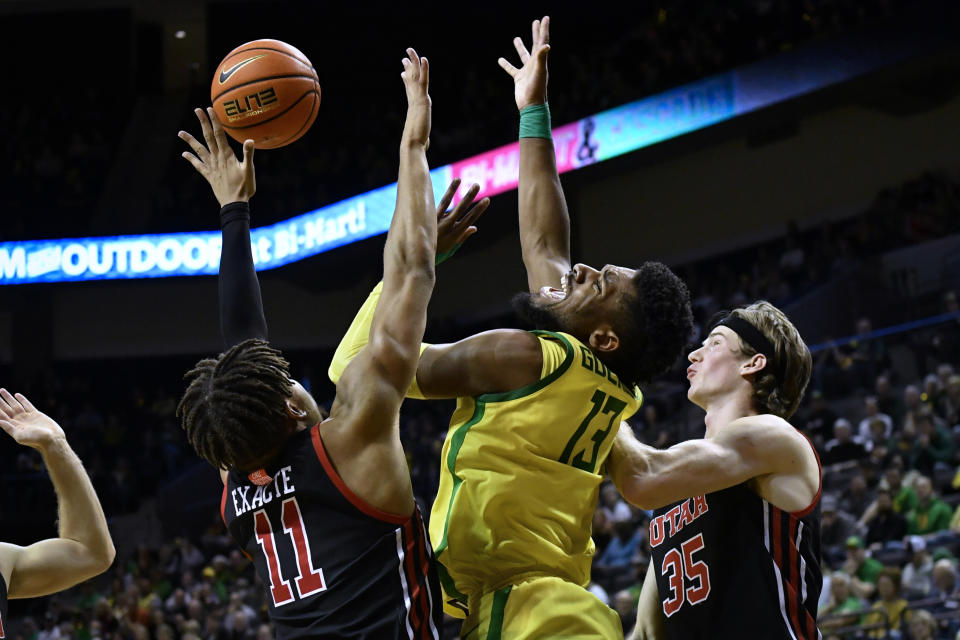 Oregon forward Quincy Guerrier (13) is defended by Utah guard Wilguens Exacte Jr. (11) and center Branden Carlson (35) during the first half of an NCAA college basketball game Saturday, Jan. 28, 2023, in Eugene, Ore. (AP Photo/Andy Nelson)