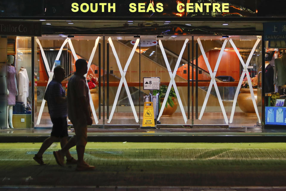 Residents walk past a shopping centre with its glass doors taped as a precaution against the approaching Super Typhoon Saola, early in the morning, in Hong Kong, on Friday, Sept. 1, 2023. The Hong Kong Observatory raised a No. 8 typhoon signal, the third-highest warning under the city's weather system, early Friday, and schools are suspended. (AP Photo/Daniel Ceng)