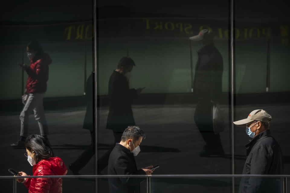 People wearing face masks are reflected in windows as they walk at a shopping and office complex in Beijing, Wednesday, March 1, 2023. (AP Photo/Mark Schiefelbein)