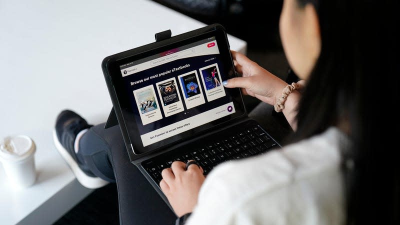 A student with feet up on the table reviewing e-Textbooks on Pearson+