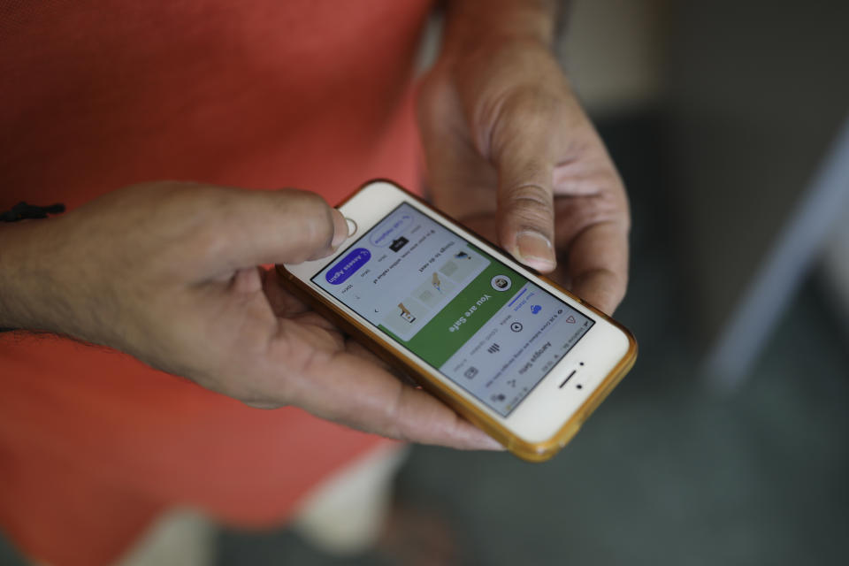 In this Thursday, May 7, 2020 photo, an Indian man uses Aarogya Setu app on his mobile phone in New Delhi, India. In April, India launched the Aarogya Setu app, which helps people identify whether they have been near someone who tested positive for the virus. Since then, the app has been downloaded more than 90 million times in a country with a smartphone user base of about 500 million. To popularize it, a campaign featuring Bollywood celebrities was launched.(AP Photo/Altaf Qadri)