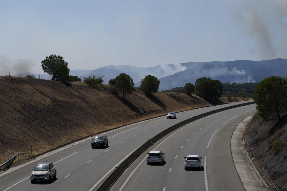 Cars drives on a highway while smoke billows from the forest near La Garde-Freinet, southern France, Tuesday, Aug. 17, 2021. Thousands of people were evacuated from homes and vacation spots near the French Riviera as firefighters battled a fire racing through surrounding forests Tuesday, the latest of several wildfires that have swept the Mediterranean region.(AP Photo/Daniel Cole)