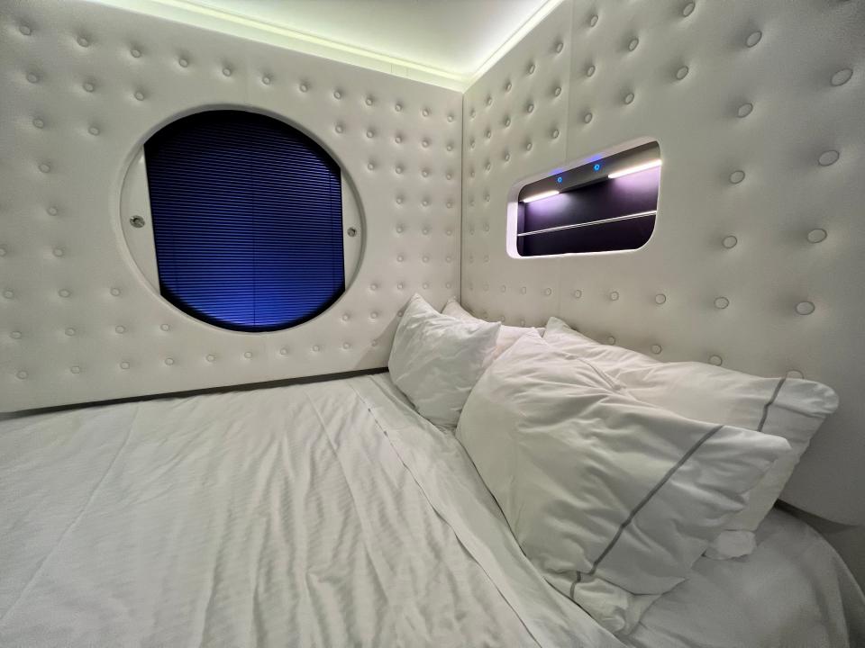 Norwegian Getaway lighting fixtures, close up of bed with circular window on the left and overhead lighting on the right