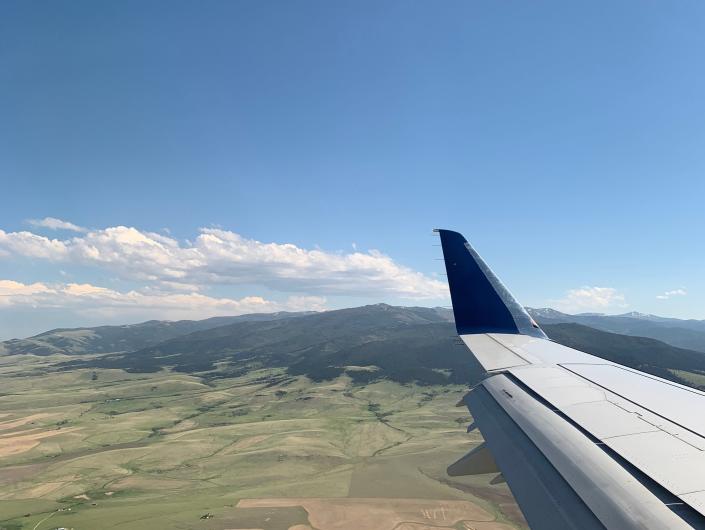 A photo of a plane wing over fields and mountains in Montana.
