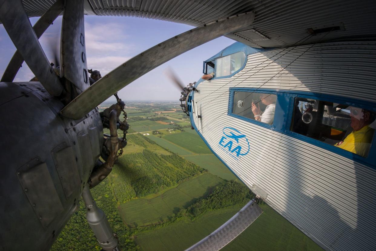 Passengers look out of the Experimental Aircraft Association's Ford Tri-Motor as it flies over a countryside.