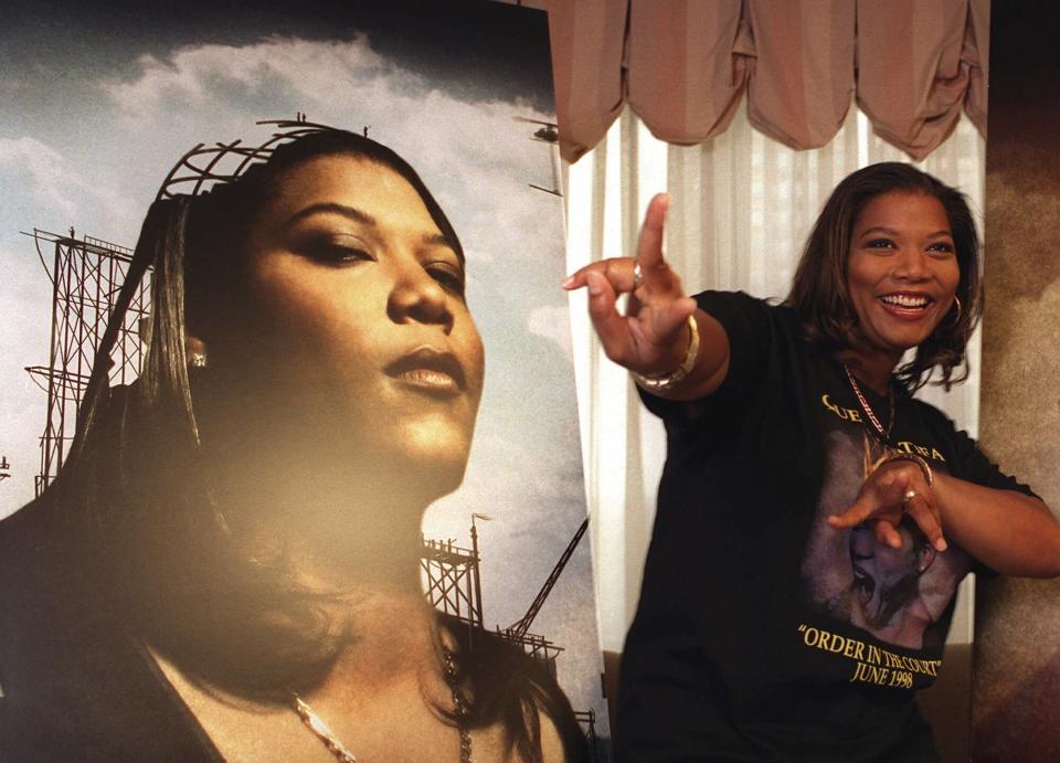 FILE - Rap singer and actress Queen Latifah gestures next to a poster of herself at a New York hotel, May 12, 1998. Women have fought to shape their identification in hip-hop and demand recognition. At its 50th anniversary, female rappers are taking their moment to shine – while still demanding respect and facing decades-old challenges. Queen Latifah's voice was one that amplified feminist storytelling and issues during the ‘80s and early ’90s. (AP Photo/Yukio Gion, File)