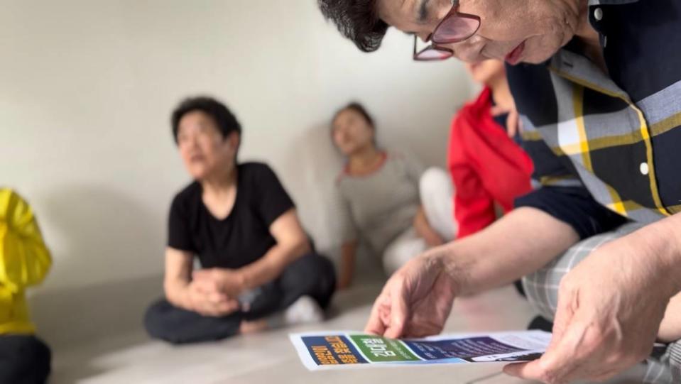 A woman at a gathering place for seniors in an old section of Hyeonjeo-dong reads the flyer containing information about Théoden Janes’s birth-family search.