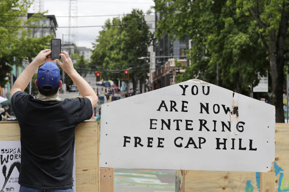 A man takes a photo over a blockade Sunday, June 21, 2020, in Seattle, where streets are blocked off in what has been named the Capitol Hill Occupied Protest zone. Police pulled back from several blocks of the city's Capitol Hill neighborhood near the Police Department's East Precinct building earlier in the month after clashes with people protesting the death of George Floyd, a Black man who died after being restrained by Minneapolis police officers on May 25. (AP Photo/Elaine Thompson)