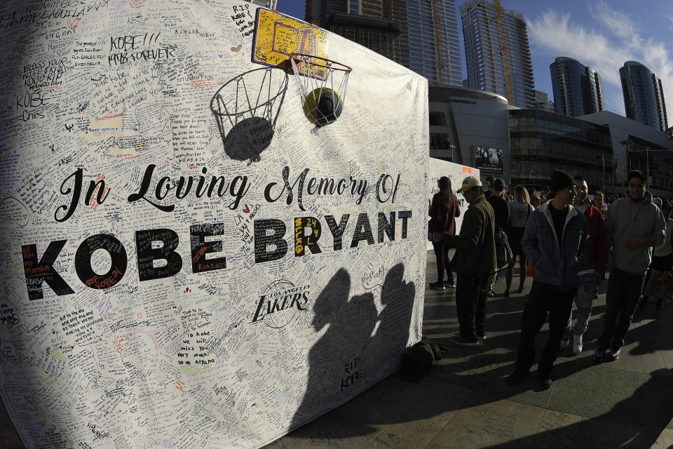 FILE - In this Jan. 28, 2020, file photo, shadows are cast on a memorial wall as fans gather at LA Live, near Staples Center where the Los Angeles Lakers play, to memorialize Kobe Bryant in Los Angeles following a helicopter crash that killed the former NBA basketball player, his 13-year-old daughter, Gianna, and seven others. (AP Photo/Mark J. Terrill, File)