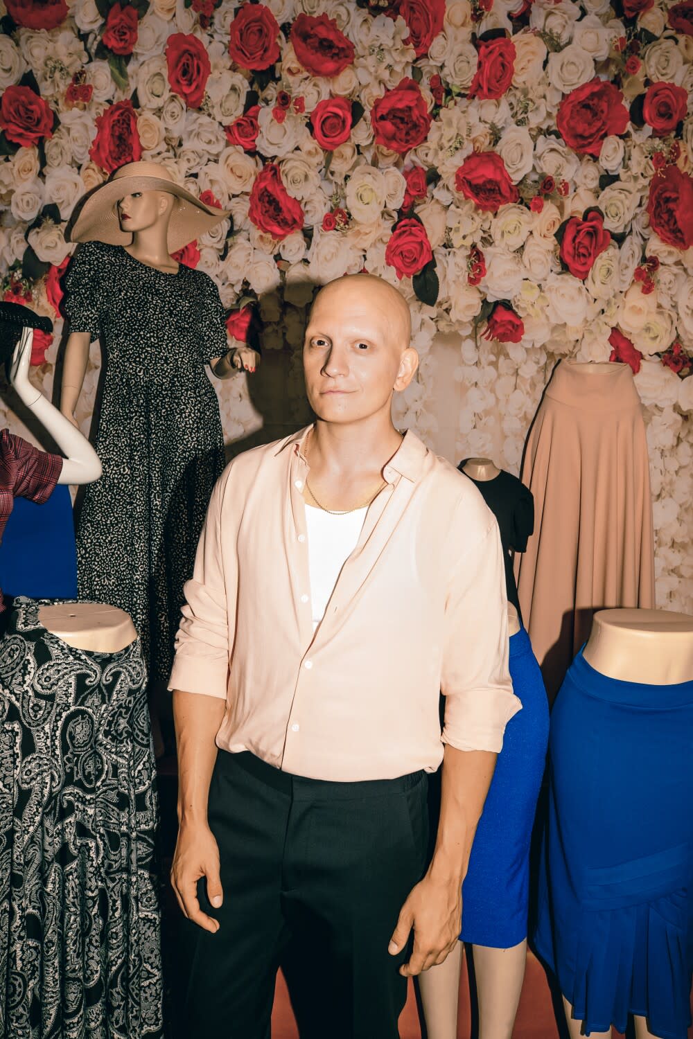 A man poses for a portrait in front of a women's clothing stall.