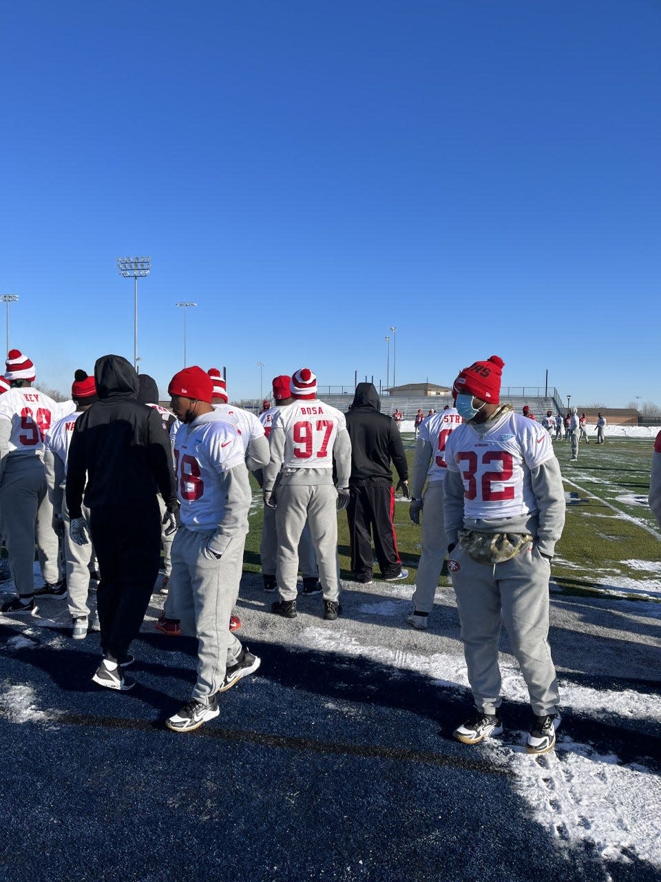 San Francisco 49ers players stand on the Bay Port High School football field on Jan. 21, the day before their NFC divisional playoff victory over the Green Bay Packers. No. 97, Nick Bosa, can be seen in the background.