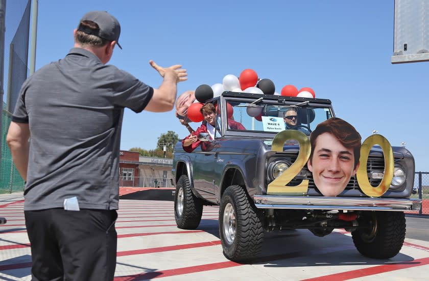 Graduate Dylan Davis is congratulated by Coach John Shanahan as he exits the Laguna Beach High drive-thru graduation at Guyer Field on Thursday.