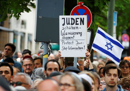 People hold a sign and Isreali flag as they attend a demonstration in front of a Jewish synagogue, to denounce an anti-Semitic attack on a young man wearing a kippa in the capital earlier this month, in Berlin, Germany, April 25, 2018. REUTERS/Fabrizio Bensch