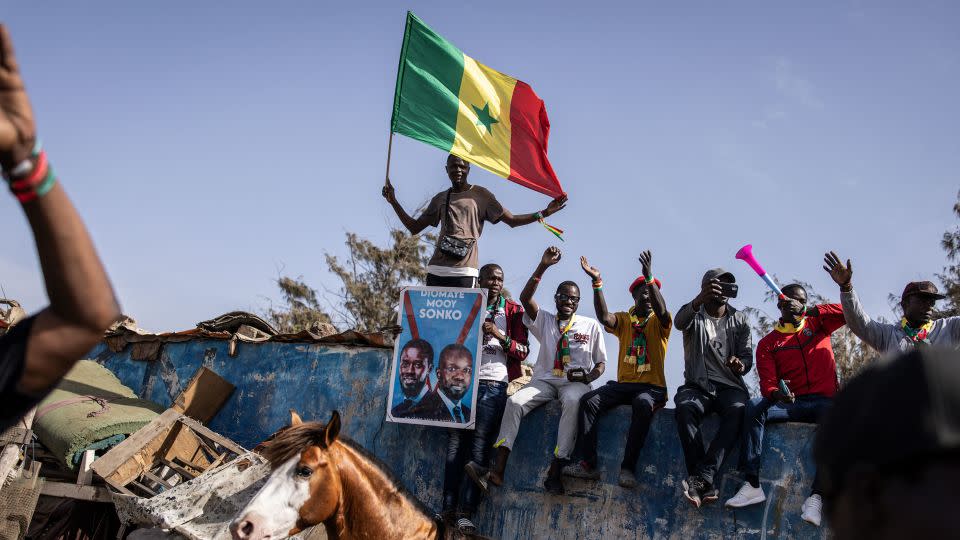 A supporter of the coalition of anti-establishment candidates holds a Senegalese flag as they sit on top of a wall during a campaign rally in Dakar on March 10, 2024. - John Wessels/AFP/Getty Images