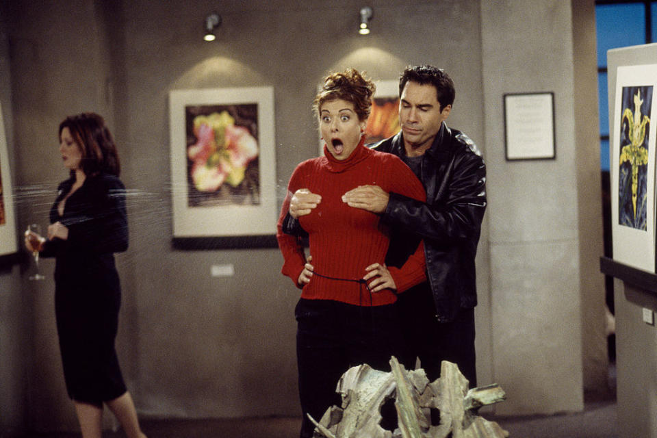 Will Truman, played by Eric McCormack, holding onto Grace's breasts from behind as liquid squirts out while they stand inside an art gallery