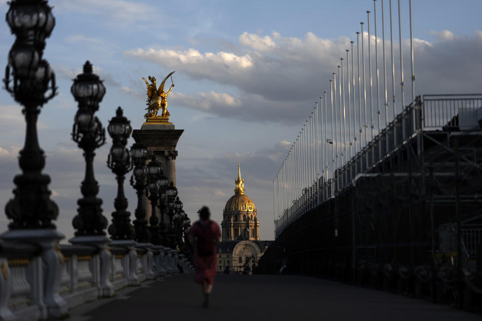 La puesta del sol frente al Hotel de los Inválidos mientras una persona cruza el puente Alexander III sobre el río Sena, el viernes 19 de julio de 2024. (AP Foto/David Goldman)