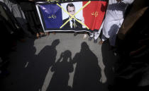 Supporters of the religious student group, Islami Jamiat Tulba, hold a representation of the French flag with a defaced image of French President Emmanuel Macron and Urdu writing which reads, "Down with France," during a protest against the publishing of caricatures of the Prophet Muhammad they deem blasphemous, in Peshawar, Pakistan, Tuesday, Oct. 27, 2020. (AP Photo/Muhammad Sajjad)