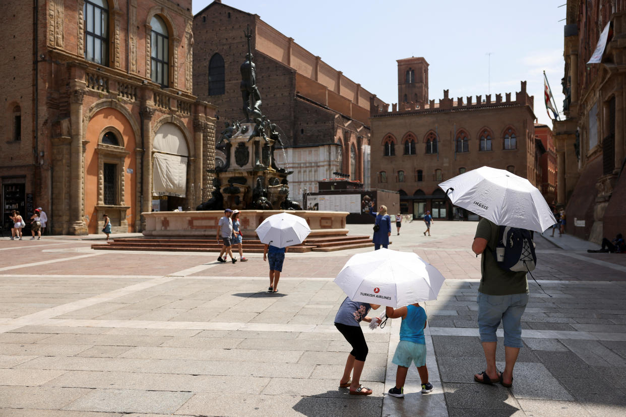 Tourists take shelters from the sun with umbrellas as they walk near Fountain of Neptune and Piazza Maggiore, during a heatwave across Italy as temperatures are expected to rise further in the coming days, in Bologna, Italy July 18, 2023. REUTERS/Claudia Greco